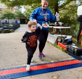 a young boy in a Spooky Shuffle shirt crossing the finish line hand in hand with a runner