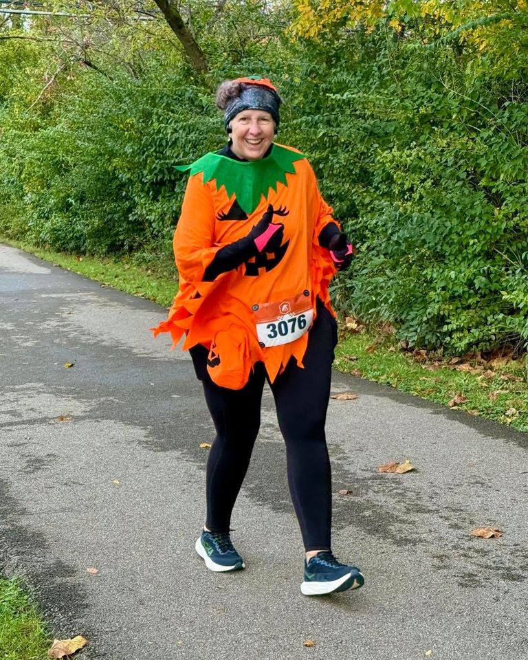 a smiling runner in a pumpkin costume giving a thumbs up on the trail